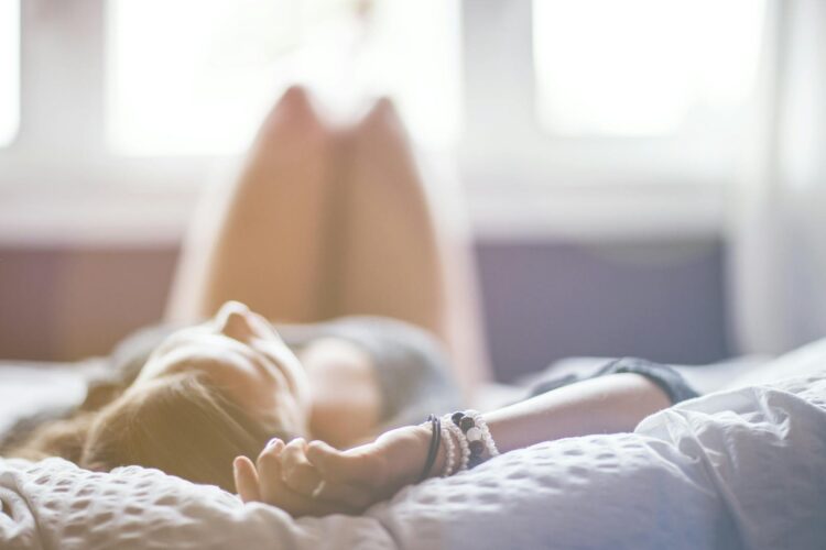 A woman lying on a bed in a peaceful, sunlit room, conveying relaxation.