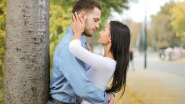 A romantic couple embracing by a tree in a vibrant autumn setting.