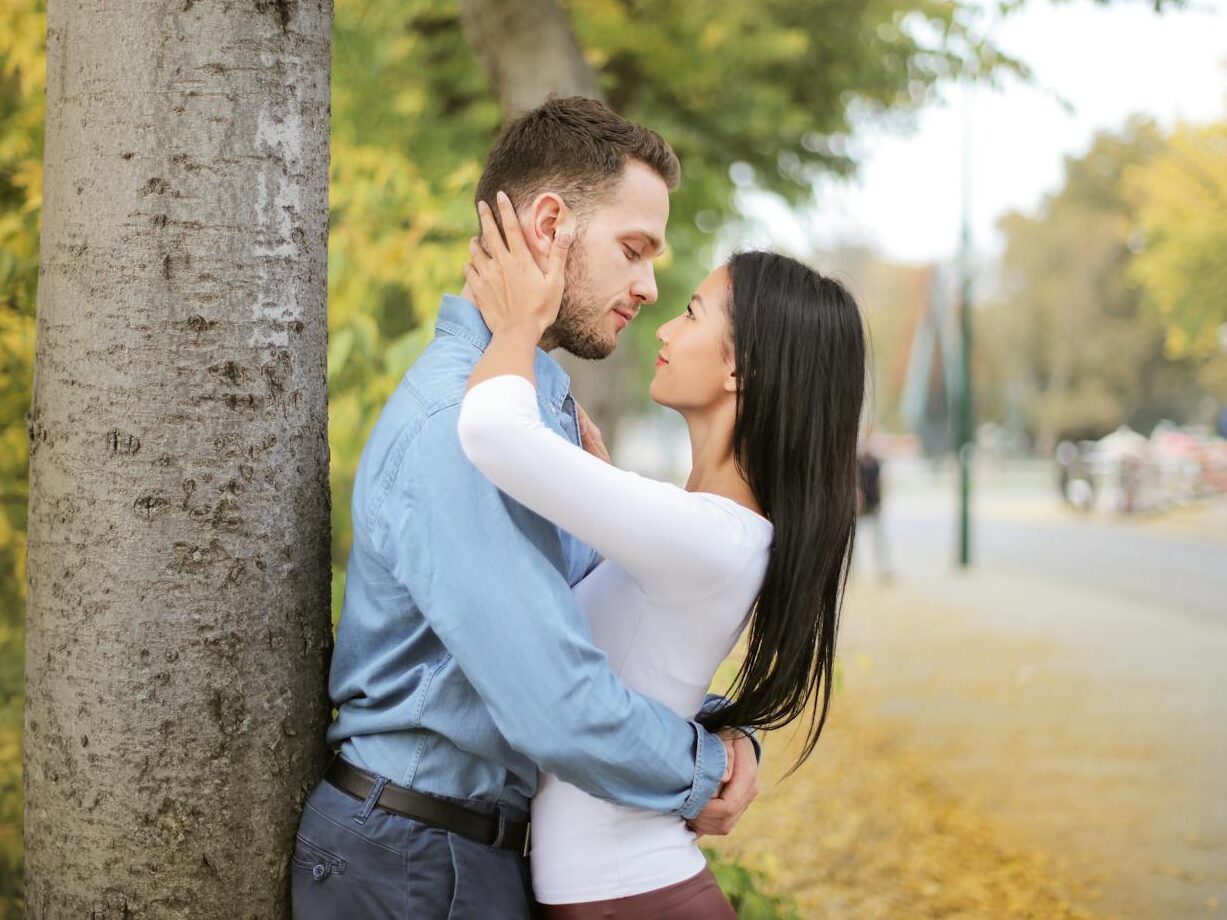 A romantic couple embracing by a tree in a vibrant autumn setting.