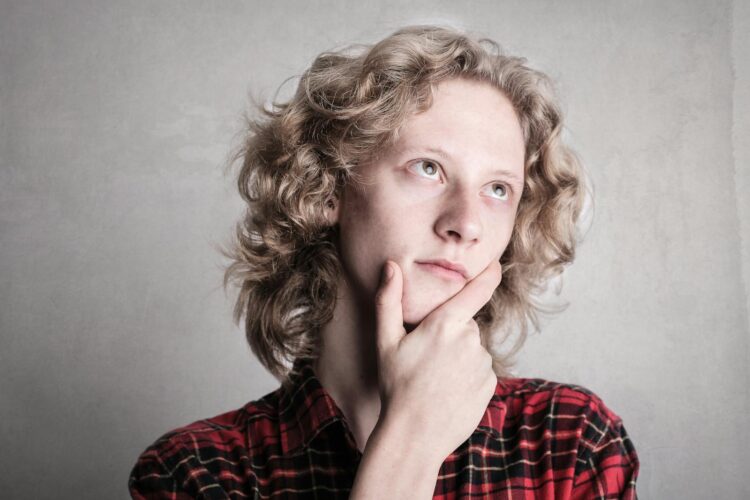 Portrait of a young adult with curly blond hair, deep in thought indoors.