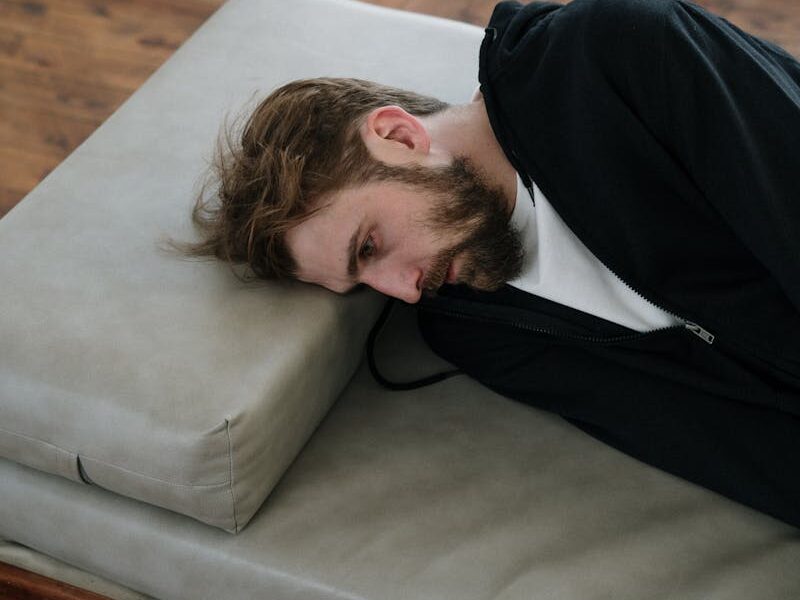 A man lies on a couch indoors, appearing deep in thought or contemplative mood.