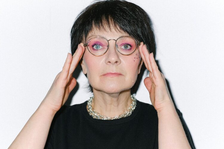 Close-up portrait of a senior woman with vibrant makeup and eyeglasses, exuding confidence.