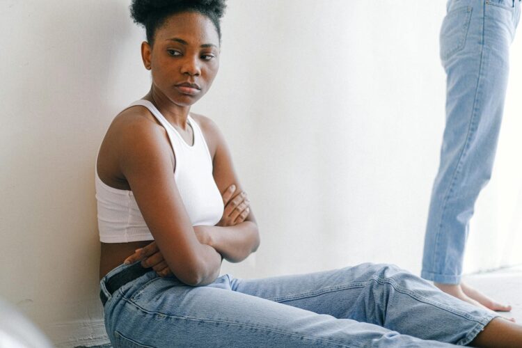 A woman sitting on the floor with crossed arms, expressing deep thought or disagreement.