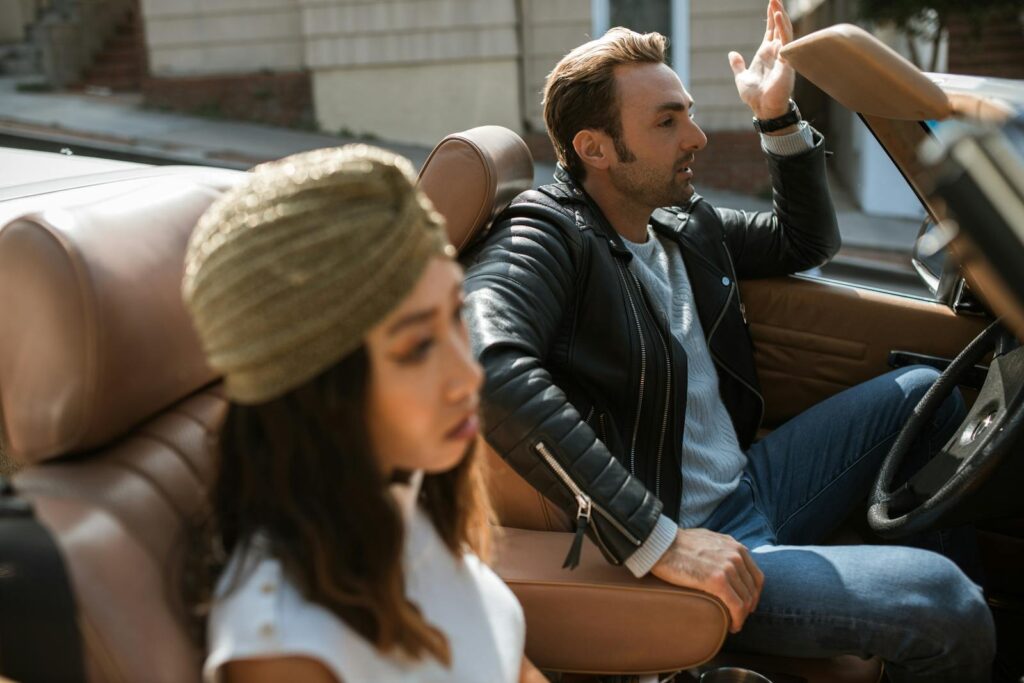A couple argues in a stylish convertible, tension evident in their expressions.