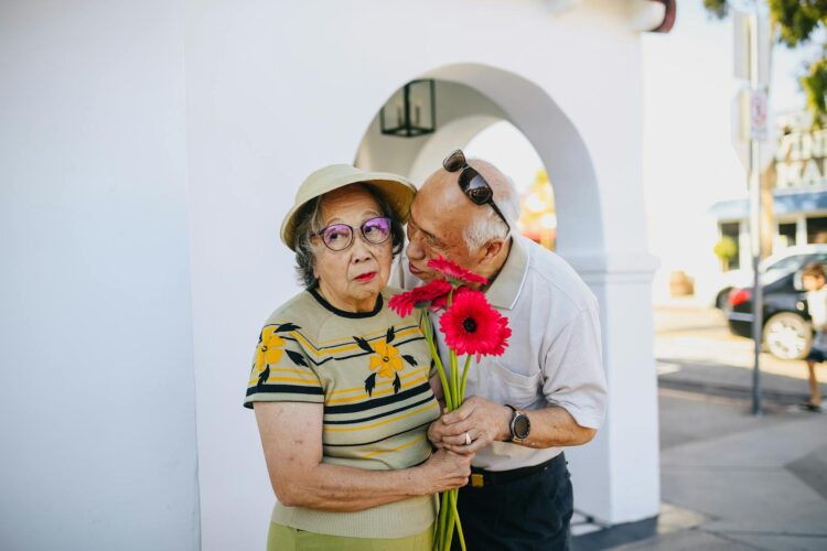 A senior Asian couple enjoying a tender moment with flowers outdoors, conveying love and affection.