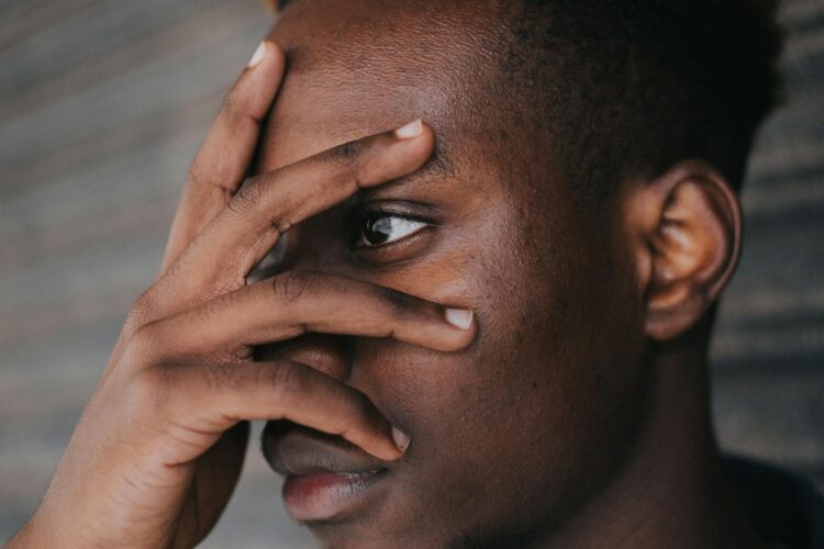 A thoughtful man peeks through his fingers in a serene outdoor setting, evoking introspection.