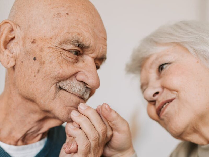 An elderly couple expressing love and affection, holding hands indoors.