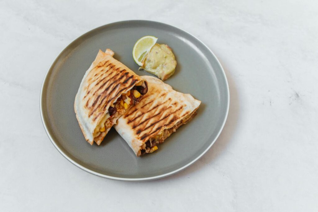 Delicious grilled quesadilla with corn, beans, and cheese on a plate, served with lemon slice.