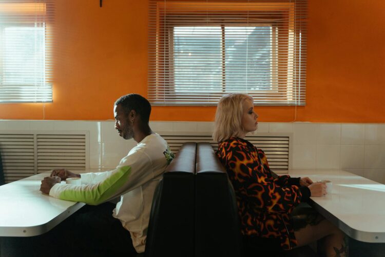 A couple sits back-to-back in a diner, reflecting a tense moment or disagreement.