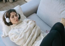A woman in a cozy sweater relaxes with headphones on a comfortable couch indoors.