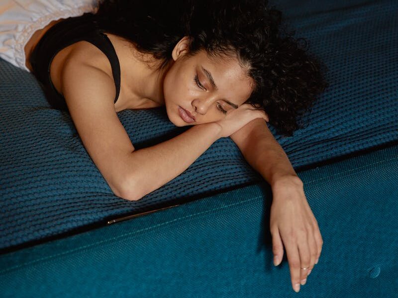 Thoughtful woman with curly hair lying on bed, expressing contemplation and calmness.