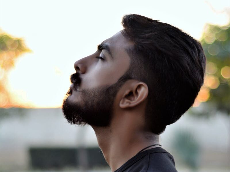 Side view portrait of a bearded man gazing upwards in an outdoor setting with blurred background.