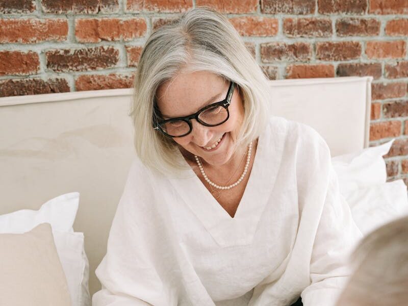 A cheerful senior woman receives a beautifully wrapped gift indoors, expressing happiness.