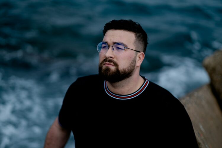 a man with a beard and glasses standing by the ocean