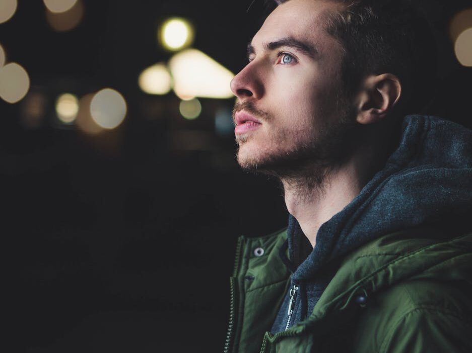 A young man in a jacket gazes thoughtfully upwards, illuminated by city lights.