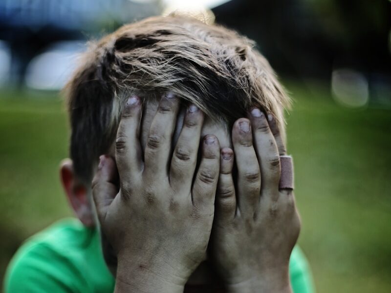 boy sitting while covering his face