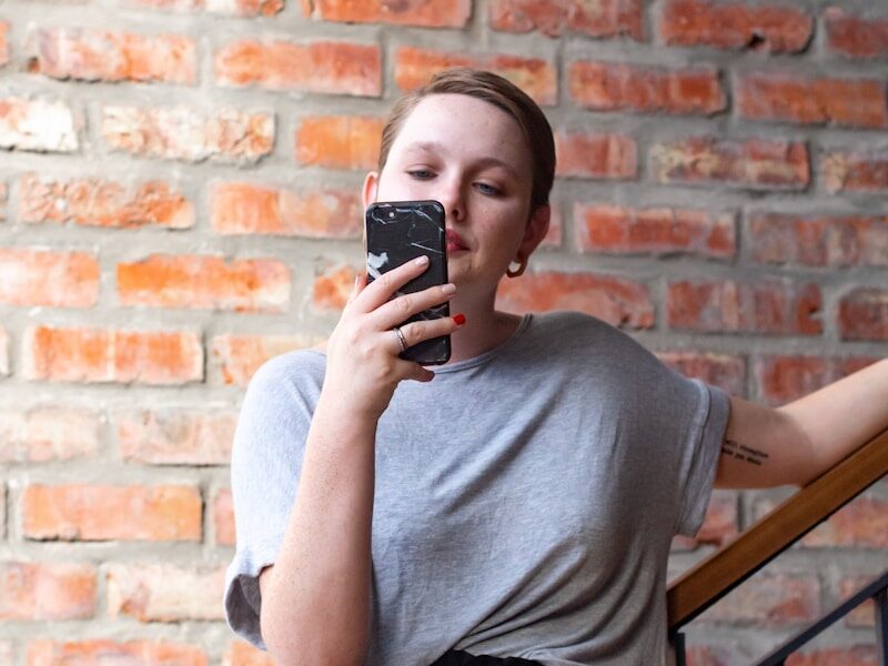 woman in gray crew neck t-shirt and black skirt holding black smartphone