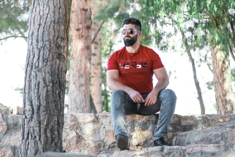 man in red crew neck t-shirt and blue denim jeans sitting on brown tree log