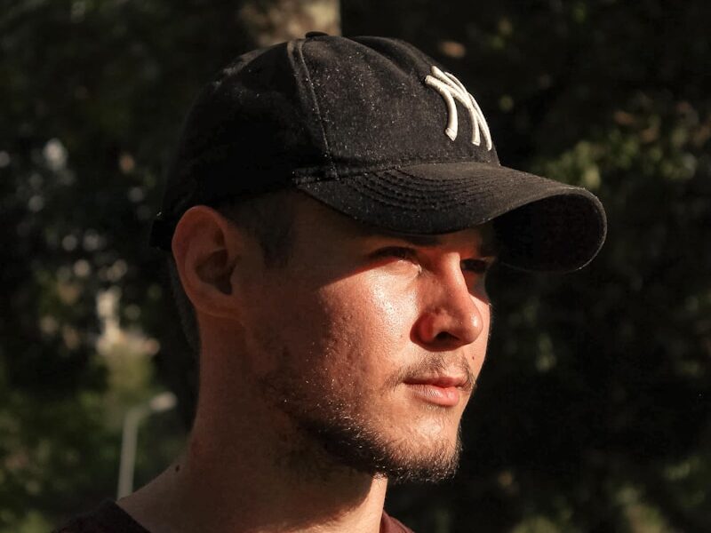 a man wearing a hat standing in front of a tree