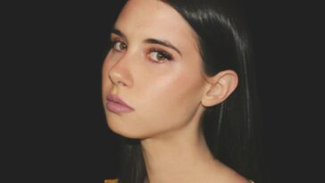 a woman with long black hair wearing a yellow top
