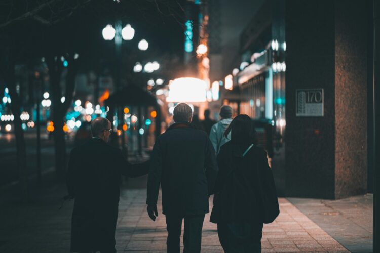 a group of people walking down a sidewalk at night