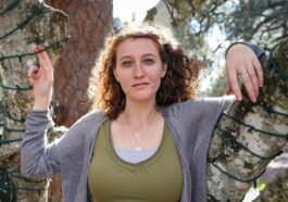 woman in gray scoop neck long sleeve shirt standing beside brown tree during daytime