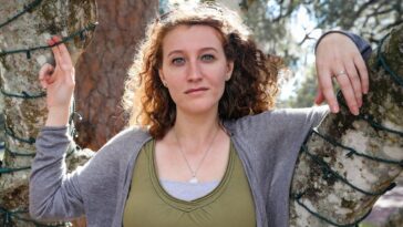 woman in gray scoop neck long sleeve shirt standing beside brown tree during daytime