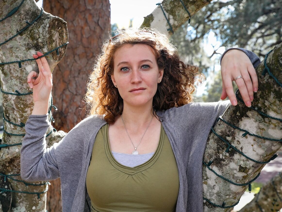 woman in gray scoop neck long sleeve shirt standing beside brown tree during daytime