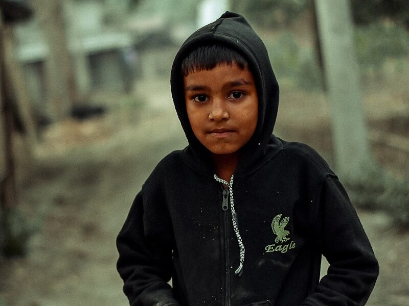 a young boy in a black hoodie standing on a dirt road