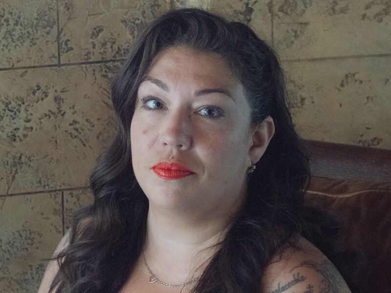 A woman with tattoos and red lipstick is posing.