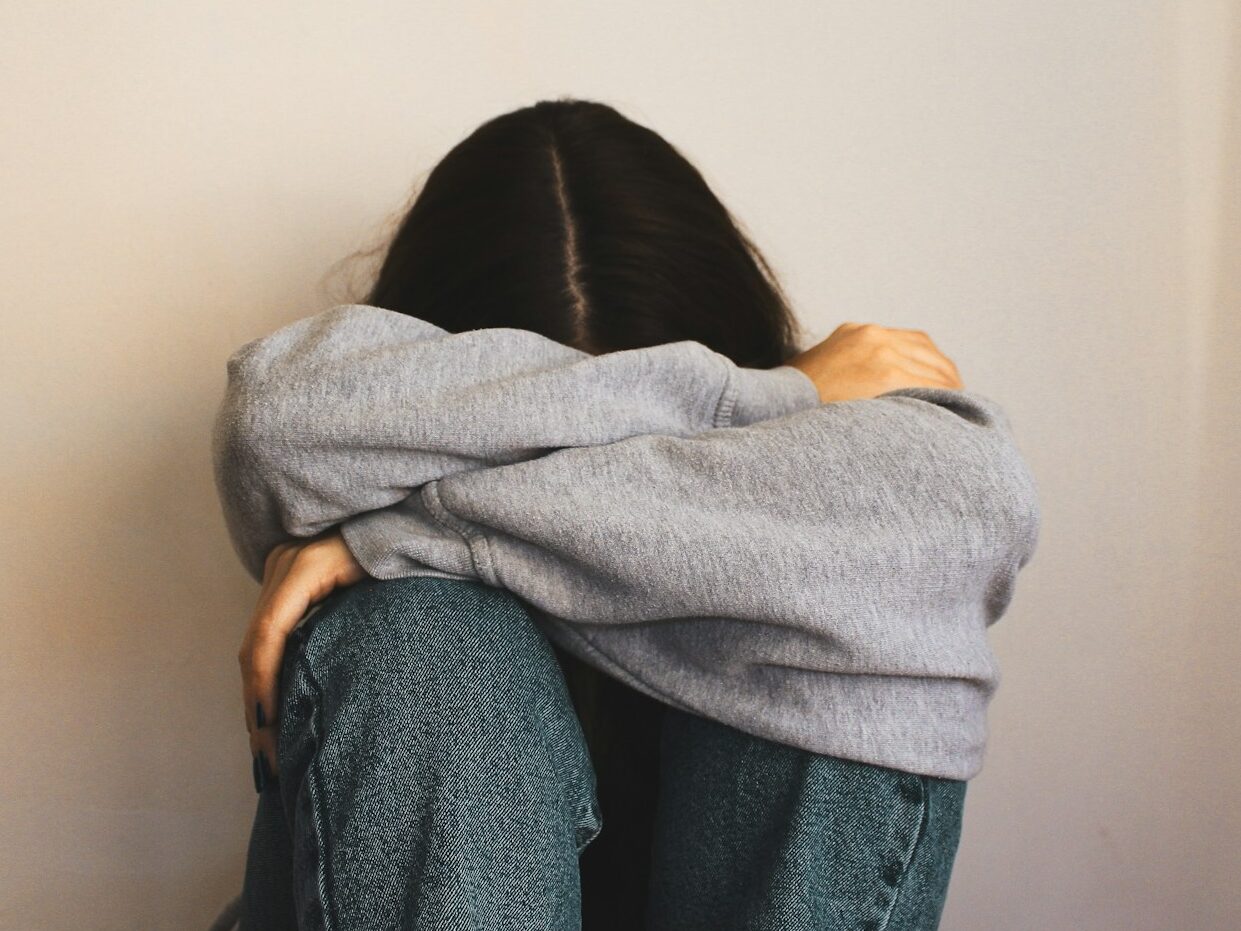 a woman sitting on the floor with her arms wrapped around her head
