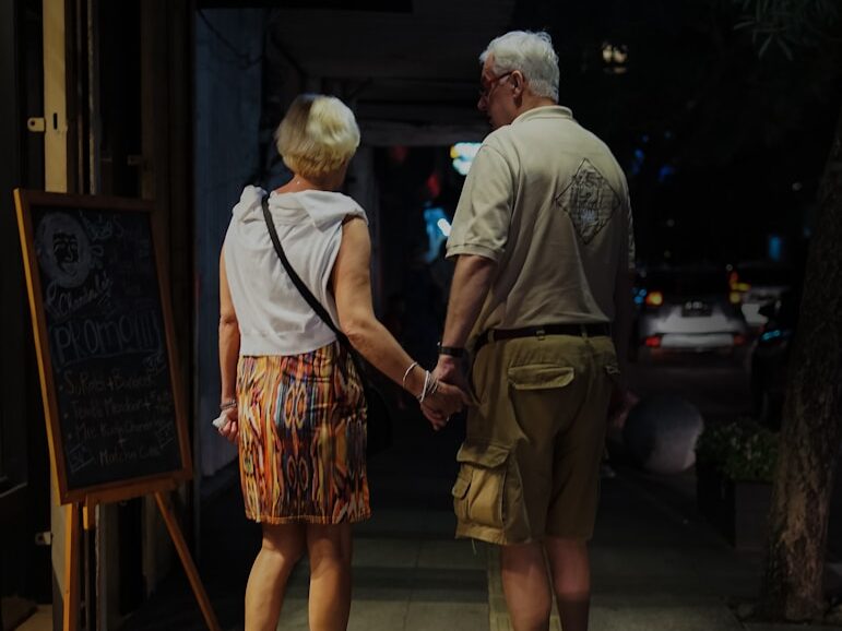 man and woman holding hands standing in front of sign