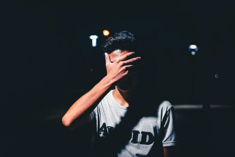 man wearing gray shirt covering his face