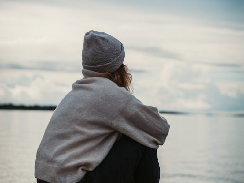 person in gray hoodie and black pants sitting on brown wooden dock during daytime