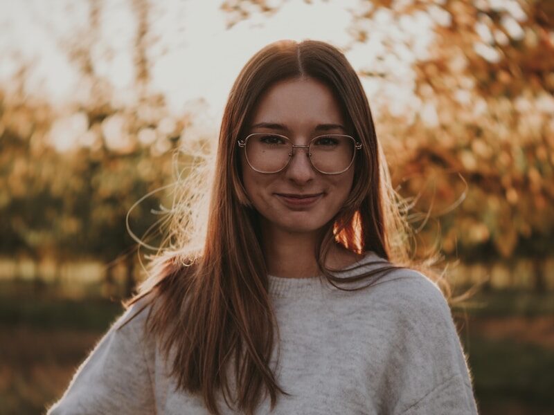 a woman wearing glasses standing in front of a tree