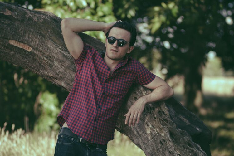 a man leaning on a tree trunk wearing sunglasses