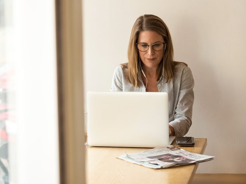 woman wearing grey striped dress shirt sitting down near brown wooden table in front of white laptop computer