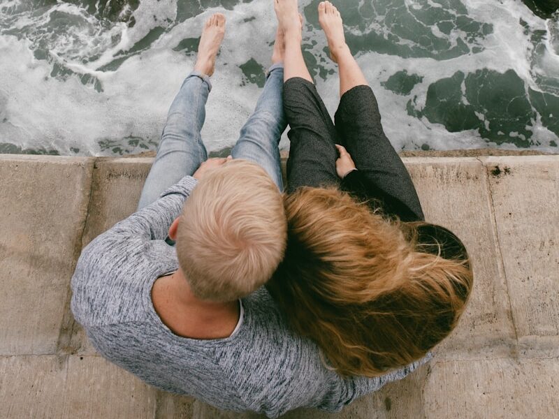 man and woman sitting on cliff near body of water