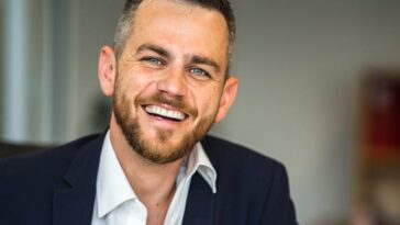 Business professional in suit smiling confidently in a modern office environment.