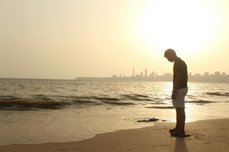 A young man stands alone on an Indian beach, silhouetted against a sunset skyline.