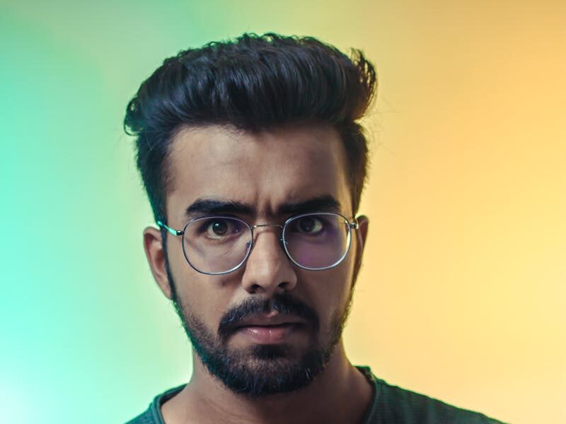 A thoughtful adult man with eyeglasses posing for a portrait with a vibrant backdrop.