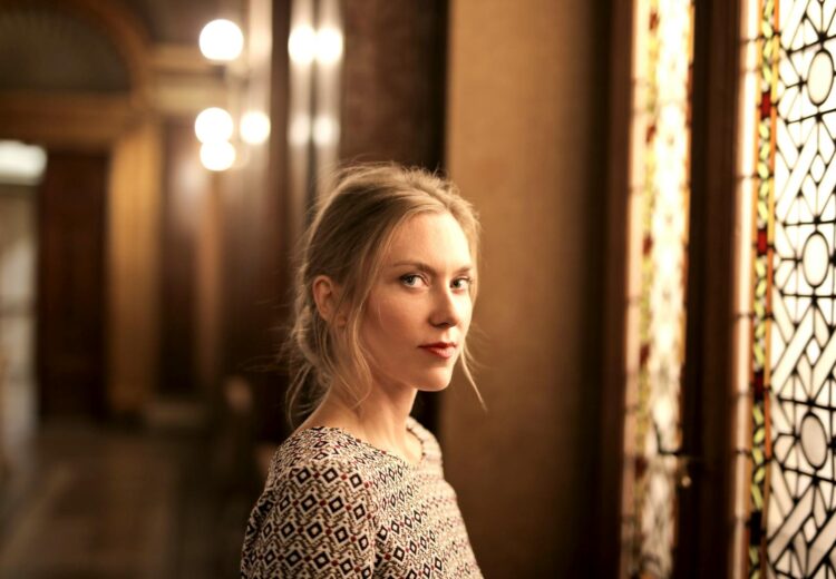 Portrait of a woman in an elegant, warm-toned room with stained glass window. Artistic and serene.