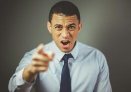 Close-up of an angry businessman in a tie expressing frustration and pointing.