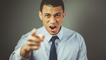 Close-up of an angry businessman in a tie expressing frustration and pointing.