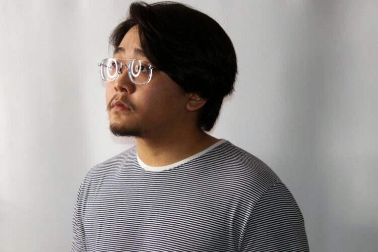 A thoughtful man wearing glasses and a striped shirt, looking to the side in a studio setting.