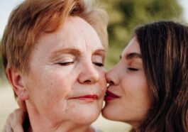A tender moment of a woman kissing her mother on the cheek outdoors, symbolizing love and connection.