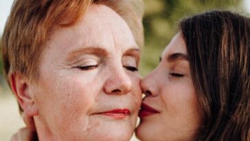 A tender moment of a woman kissing her mother on the cheek outdoors, symbolizing love and connection.