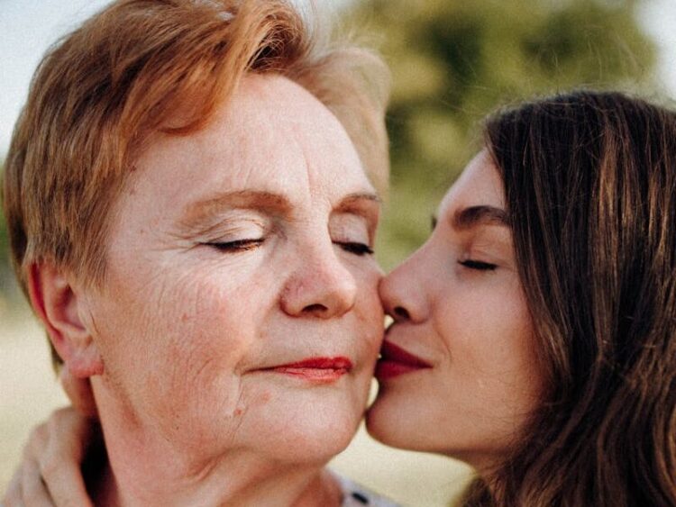 A tender moment of a woman kissing her mother on the cheek outdoors, symbolizing love and connection.
