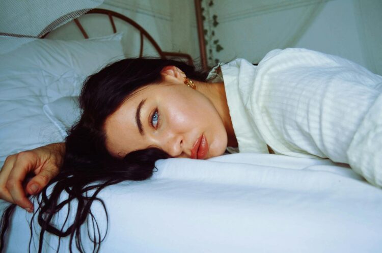 A serene portrait of a woman relaxing indoors, lying on a comfortable bed.