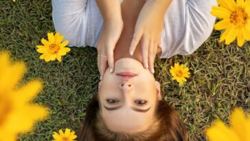 Upside down portrait of a woman lying on grass with yellow flowers in her hair.